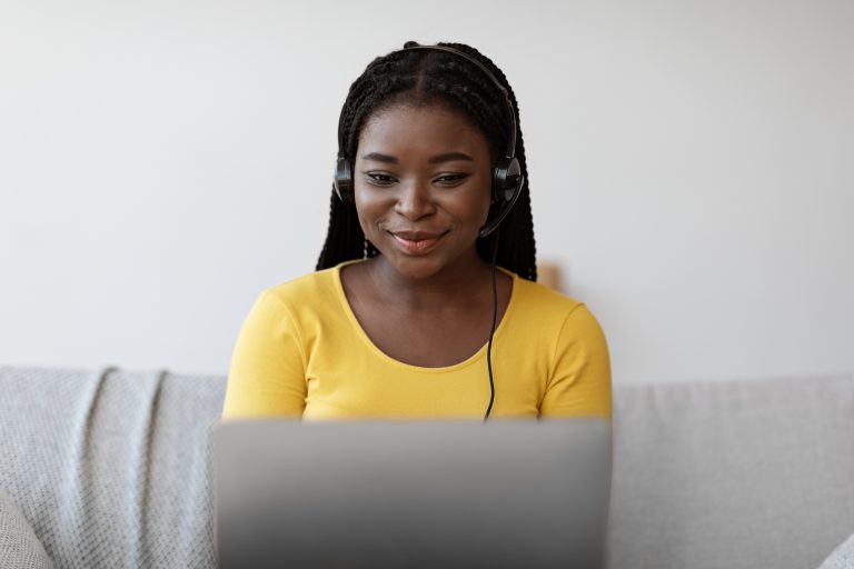 Smiling african american woman in headset watching webinar on laptop at home
