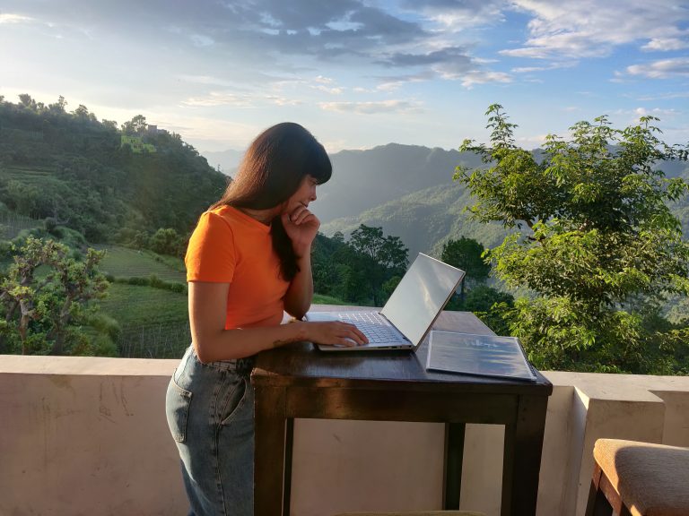 Woman looking at laptop outdoors with a beautiful backdrop of hills and trees