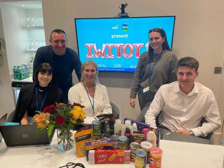 A team sat around a desk with snacks and a screen behind then showing IWITOT