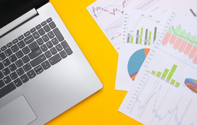 A laptop on a yellow background, next to paper containing statistics